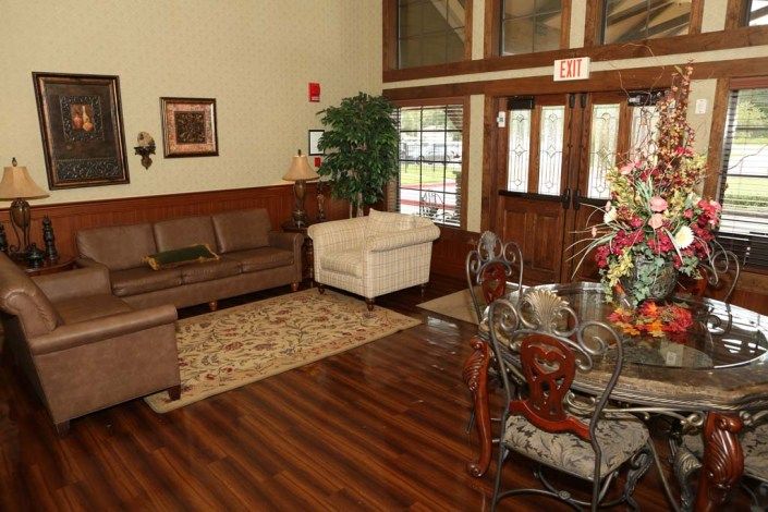 A cozy living room with a sofa, armchair, and dining table on a wooden floor, complemented by indoor plants and wall decorations.
