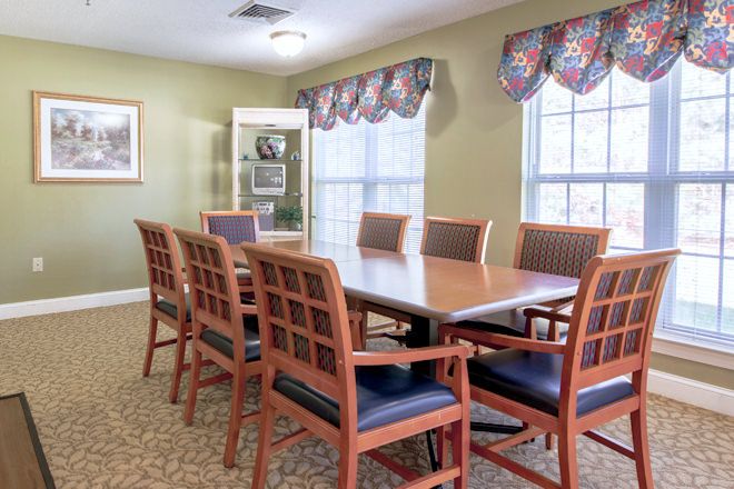 A well-furnished conference room with a wooden meeting table and cushioned chairs, illuminated by natural light from large windows.