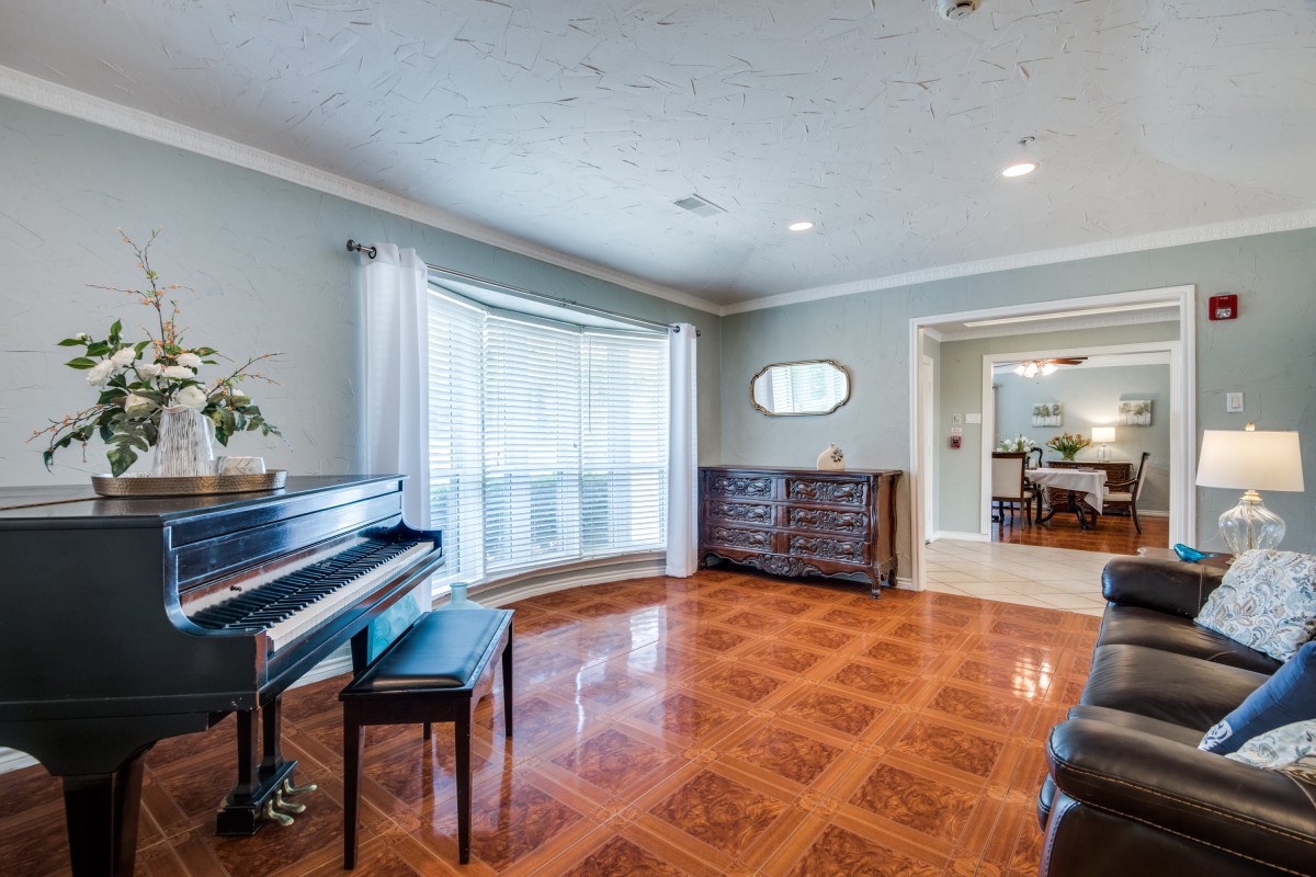A spacious living room featuring a piano, hardwood floors, and large windows with drapes.