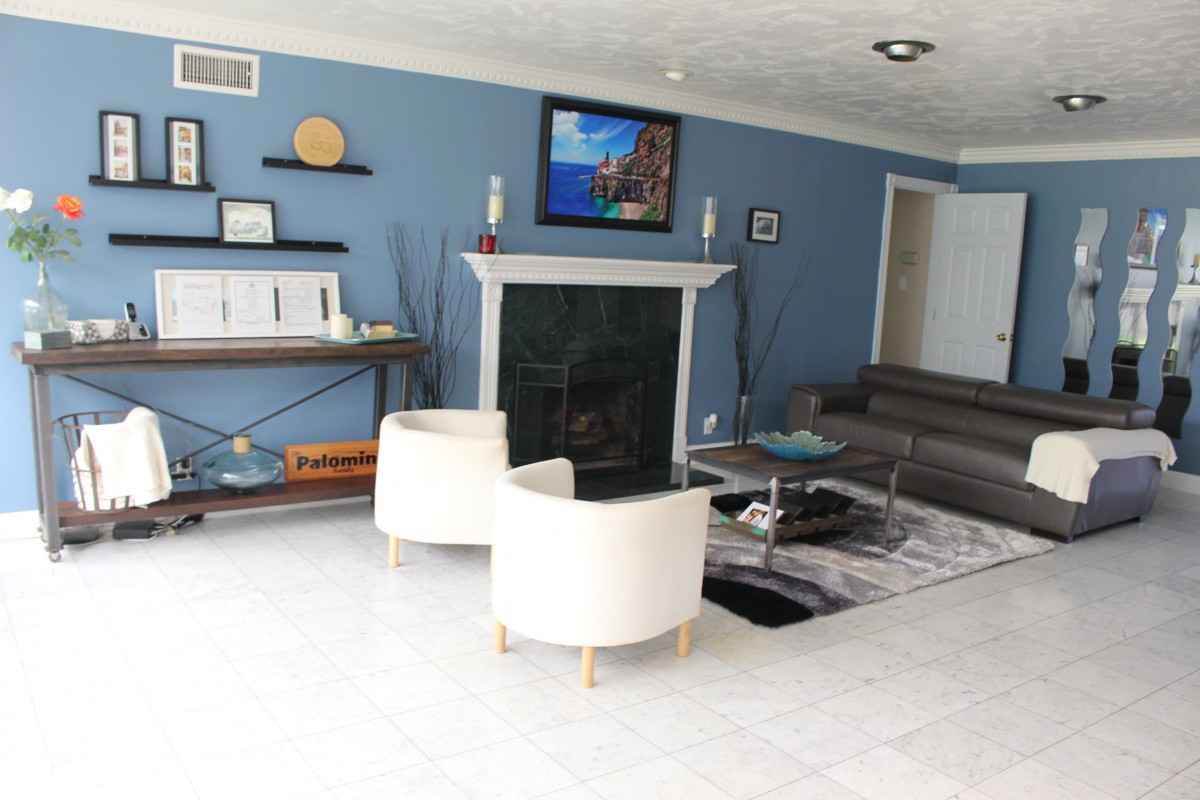 A modern living room with blue walls and contemporary furniture, featuring a fireplace and a mounted television.