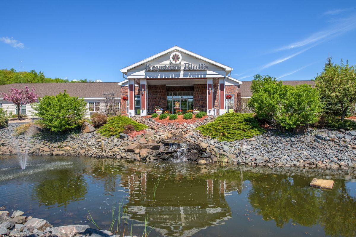 A charming building with a symmetrical facade surrounded by lush greenery and a tranquil pond reflecting its structure.