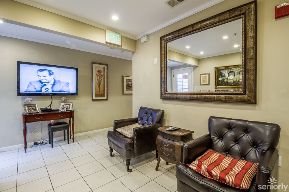 A comfortable waiting room featuring leather chairs, a large mirror, and a wall-mounted television.