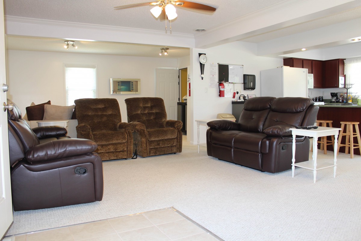 A spacious living room with multiple recliners and a sofa, featuring neutral-colored walls and carpeting.
