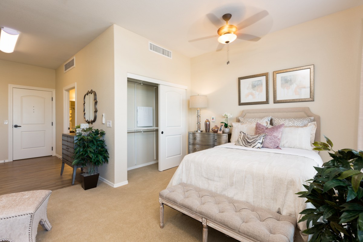 A cozy and elegantly decorated bedroom featuring a ceiling fan, artwork on the walls, and a plush bed with soft bedding.