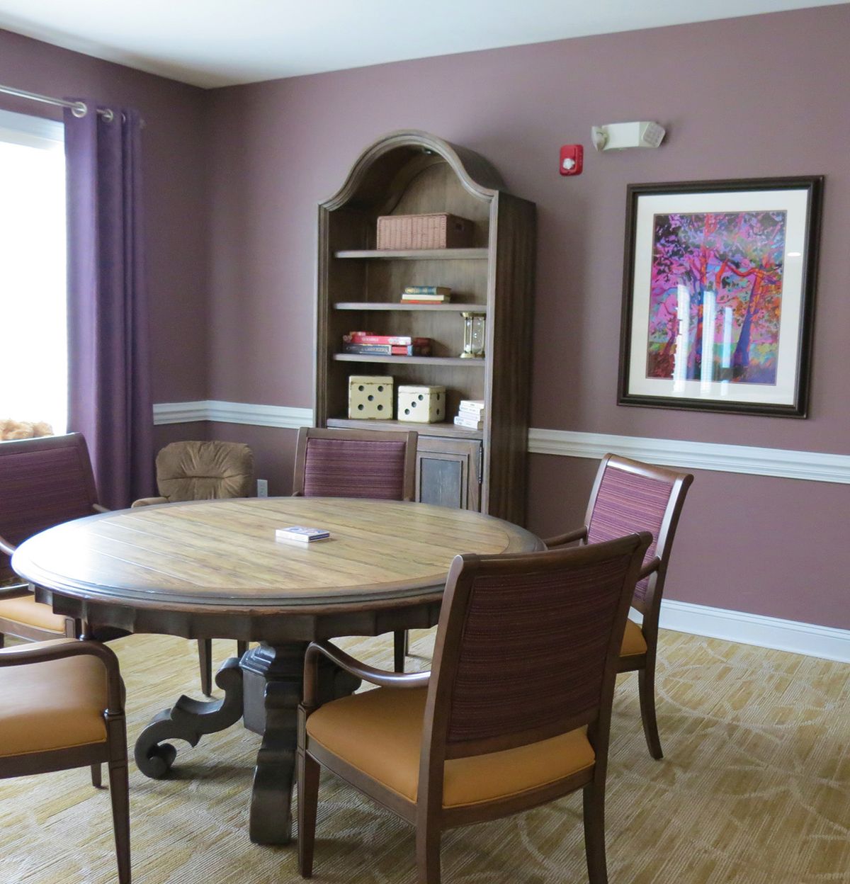 A cozy room with a round wooden table, surrounded by chairs, and a bookshelf against the wall.