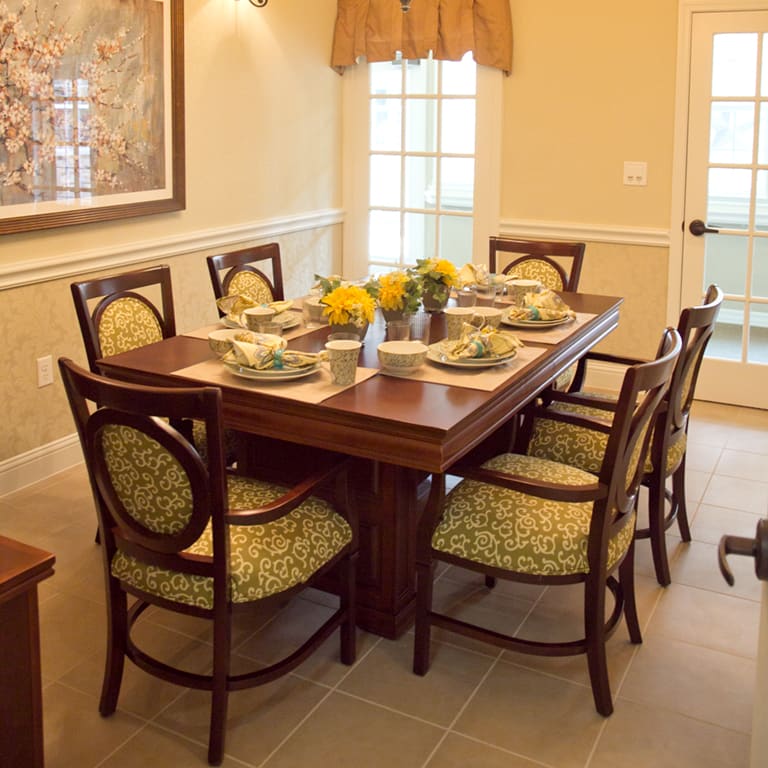 A warmly decorated dining room with a wooden dining table set for six, featuring floral centerpieces and elegant place settings.
