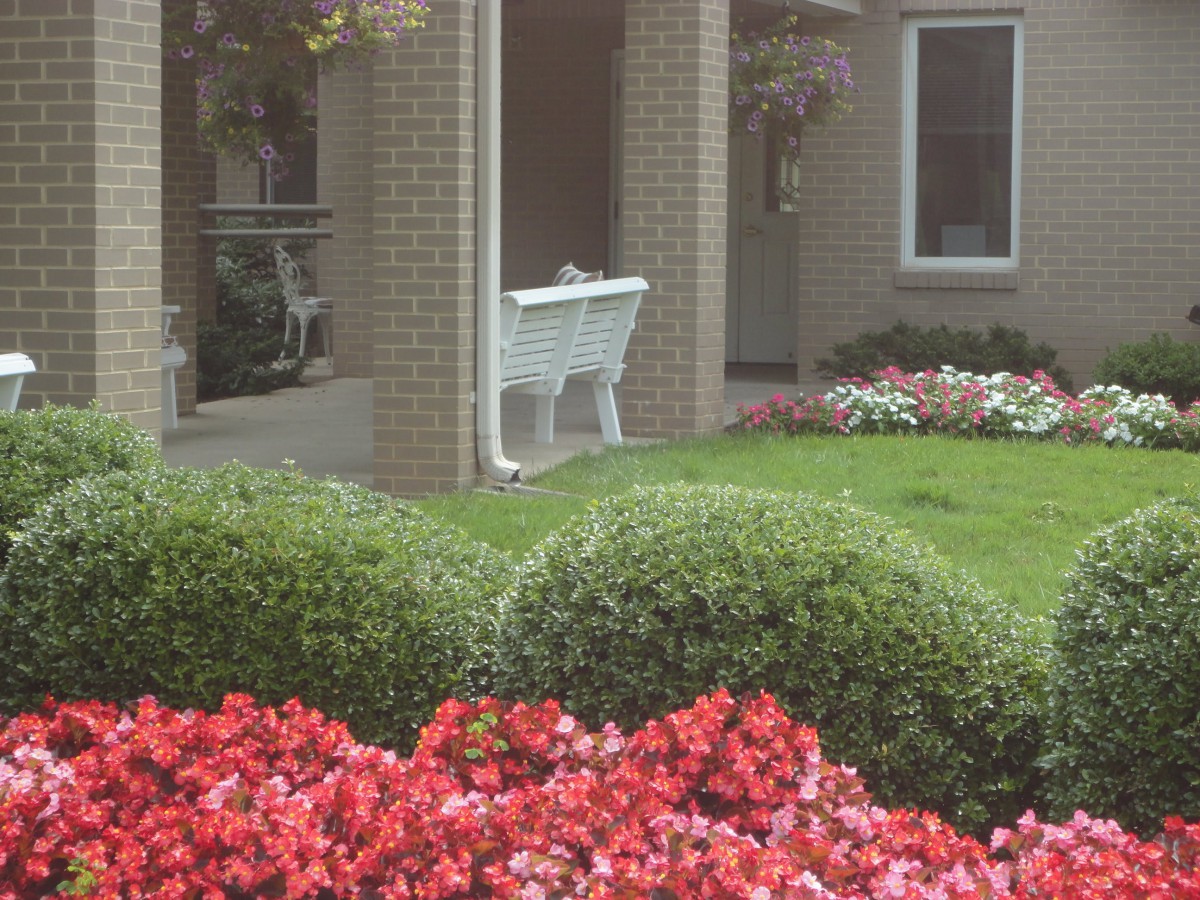 A well-maintained garden with colorful flowers and a white bench near a brick building.