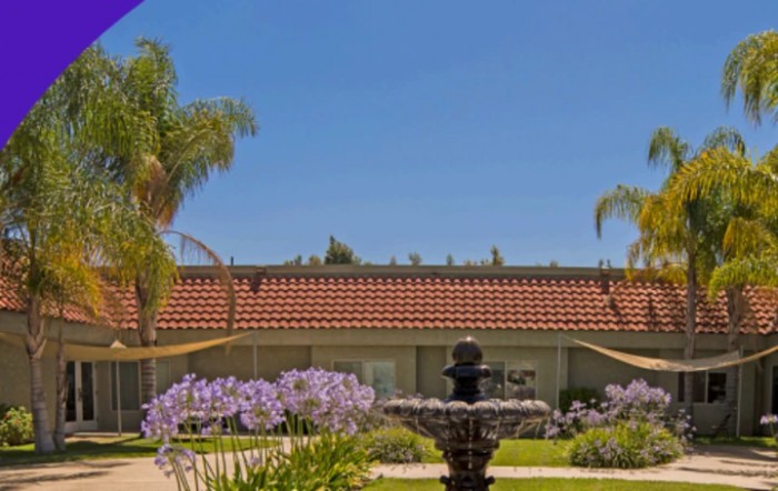 A sunny garden with a fountain and flowers in front of a house.