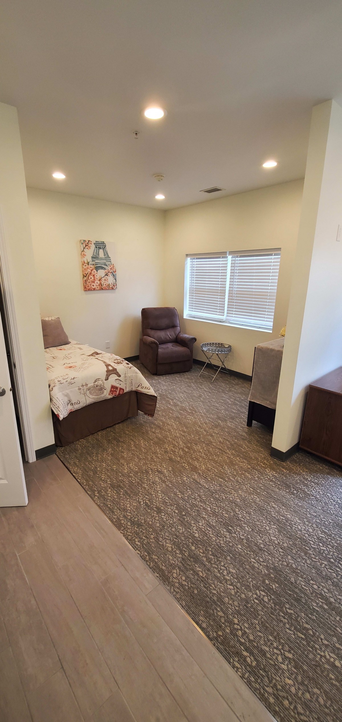 A cozy bedroom interior with a bed, reclining chair, and window.