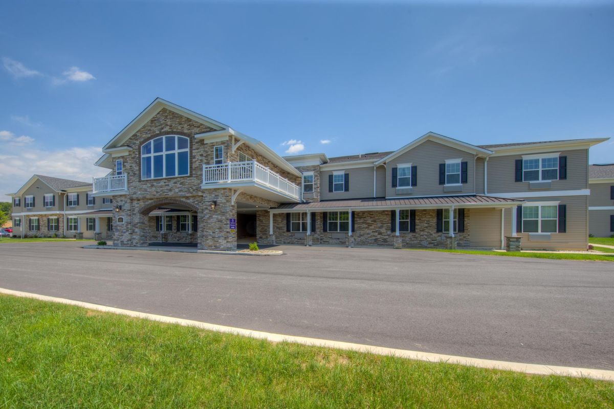 A large stone and siding house with multiple windows, a balcony, and a spacious driveway under a clear blue sky.
