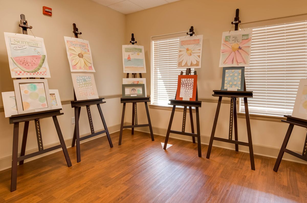 A small art exhibition displaying various paintings on easels in a well-lit room.