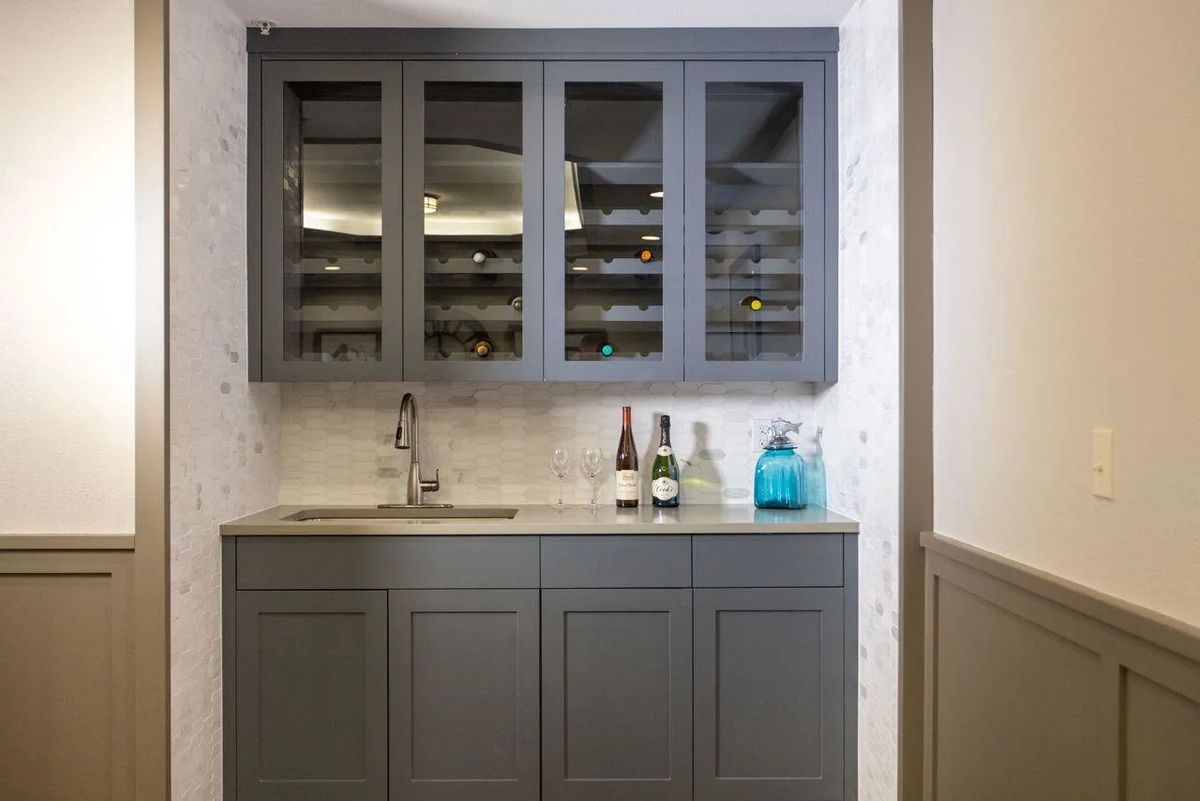 A modern kitchen setup with a grey cabinet, countertop, sink, and bottles displayed.