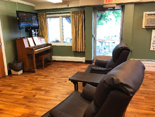 A cozy lounge area featuring comfortable seating, a piano, and natural light coming through the windows.