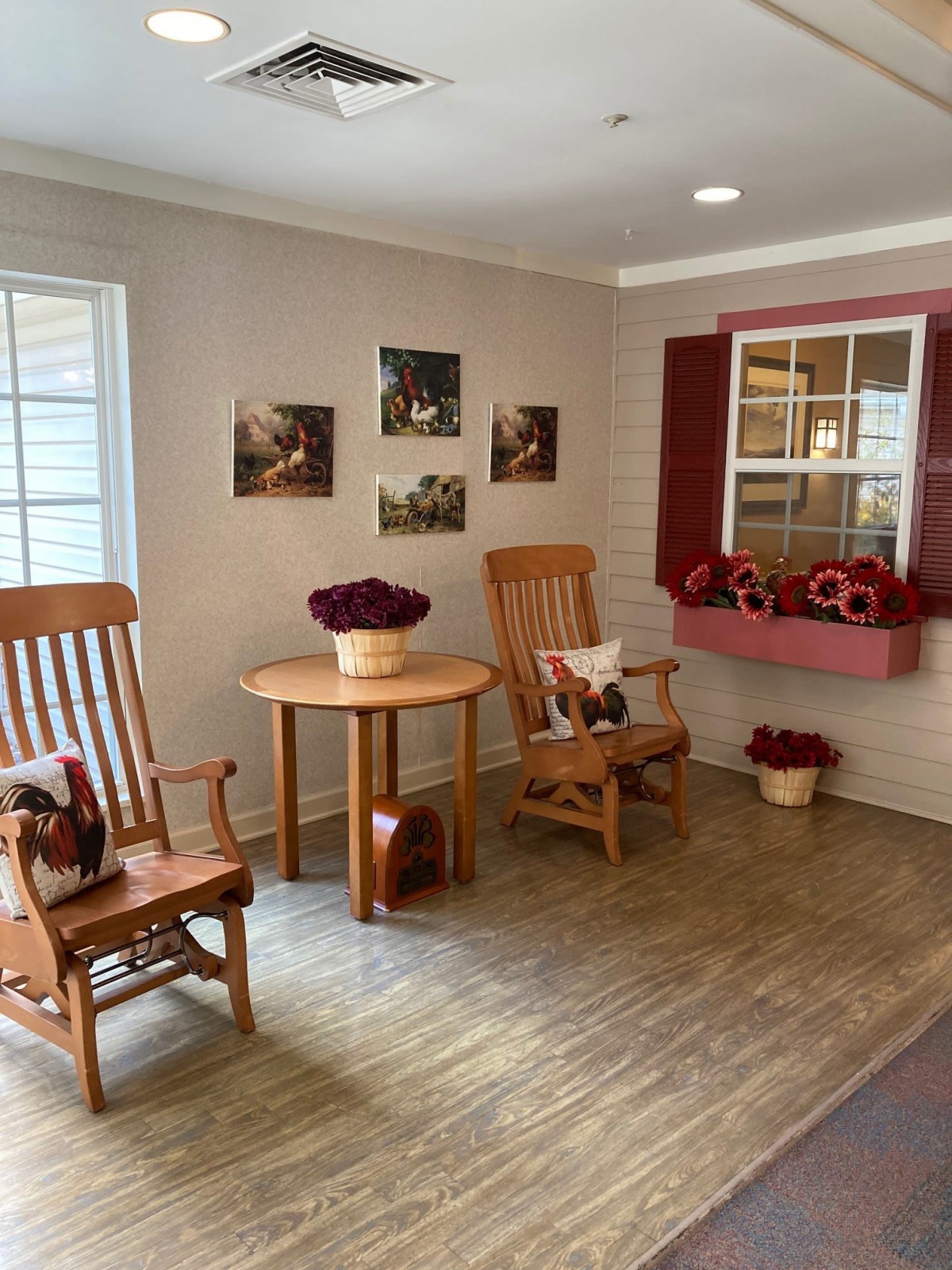 A cozy room featuring wooden rocking chairs, a small table with a flower arrangement, and decorative wall art.