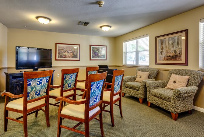 A cozy meeting room with chairs arranged in front of a television, decorated with artwork and natural light coming through the windows.