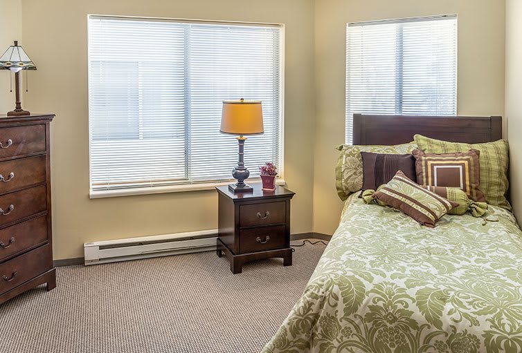 A cozy bedroom with a bed, nightstand, and lamp by the window.