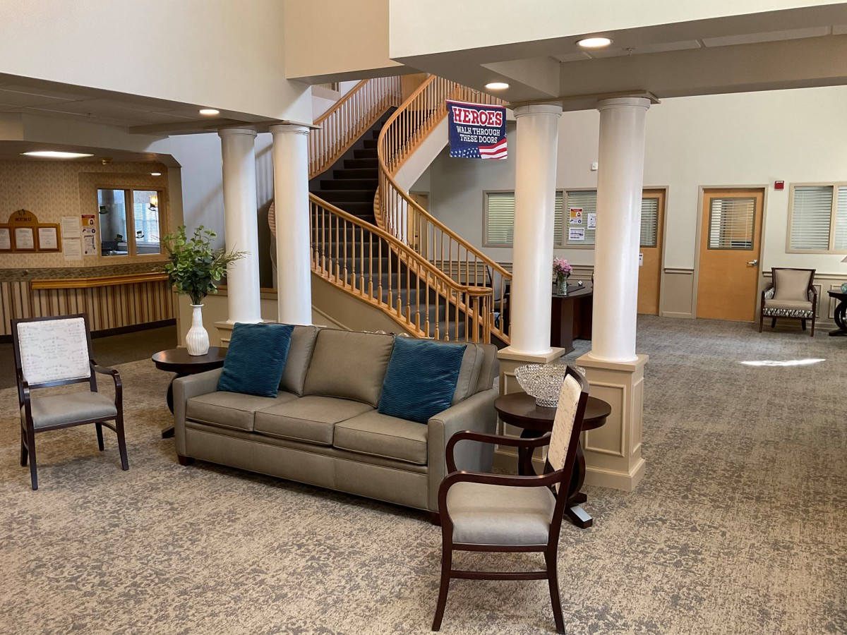 A spacious lobby featuring comfortable seating with a sofa and chairs, pillars, and a wooden spiral staircase.