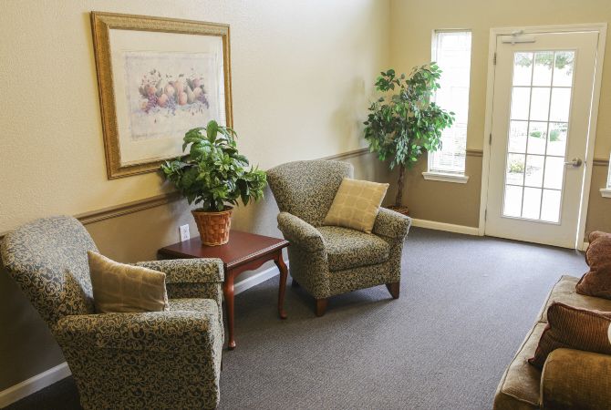 A cozy living room with two armchairs, a small table, potted plants, and a wall painting.