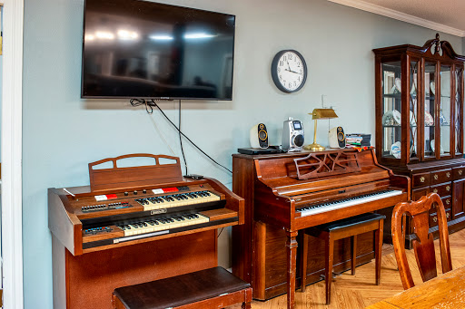 A cozy living room featuring a vintage organ and piano, along with a television and clock.