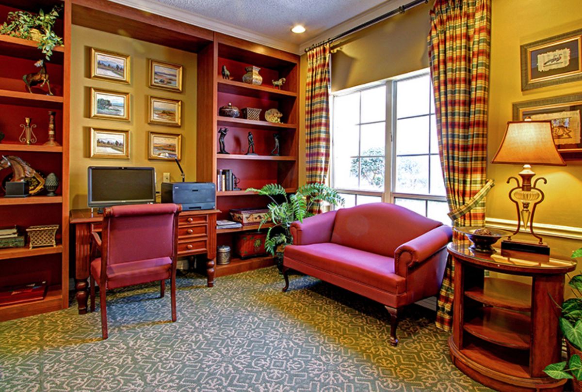 A cozy office space with a desk, computer, bookshelves, and a small sofa near a window.