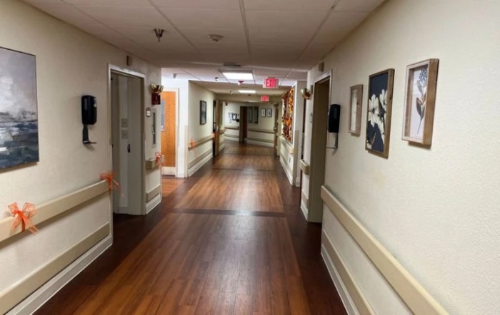 A long hospital corridor with wooden flooring and wall decorations.