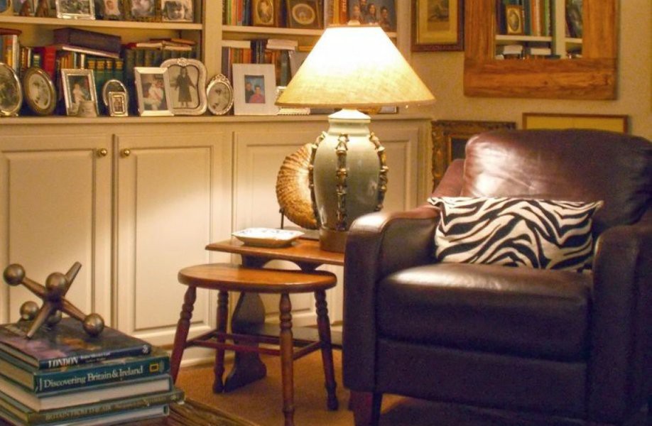 A cozy living room with a leather couch, a lamp on a side table, and shelves filled with books and framed photos.