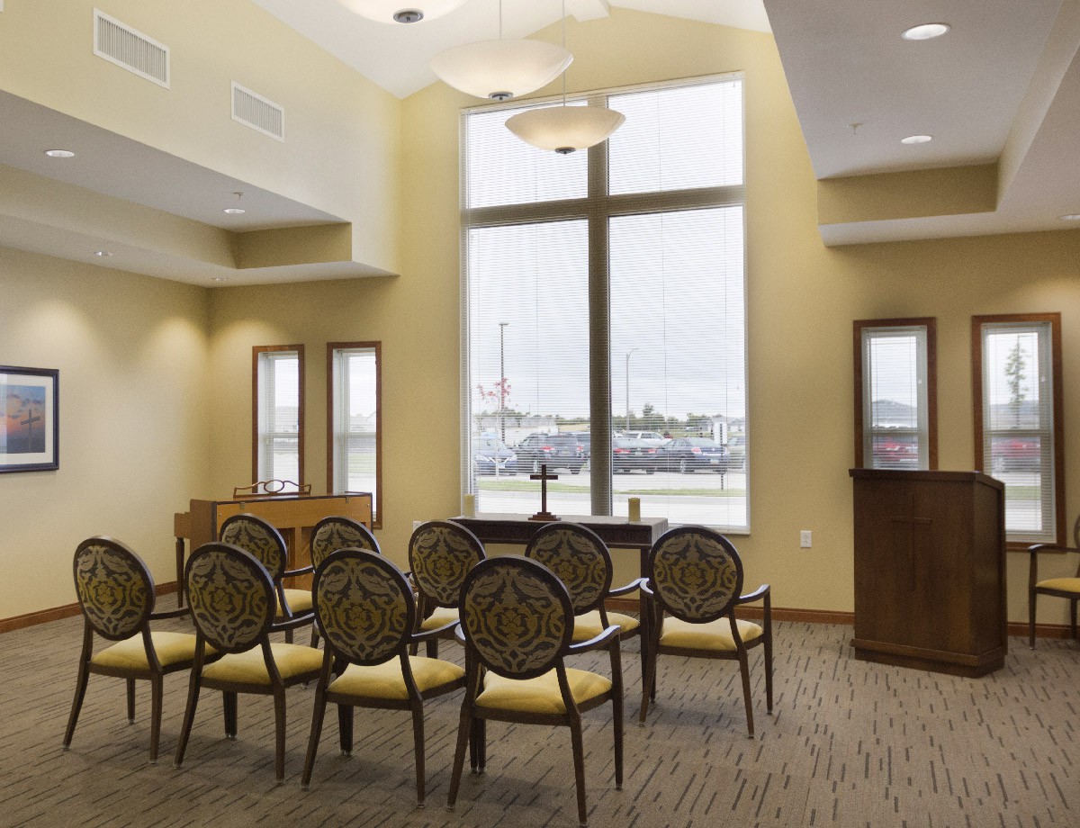A small, well-lit meeting or lecture room with chairs arranged in rows and large windows overlooking an outdoor view.