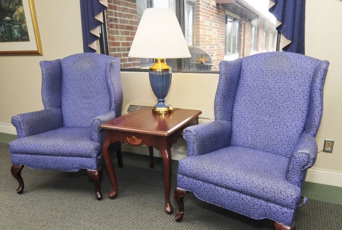 A cozy seating area with two blue armchairs and a wooden side table topped with a lamp.