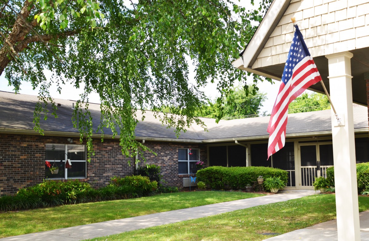 A suburban brick house with an American flag on display and a well-kept lawn.