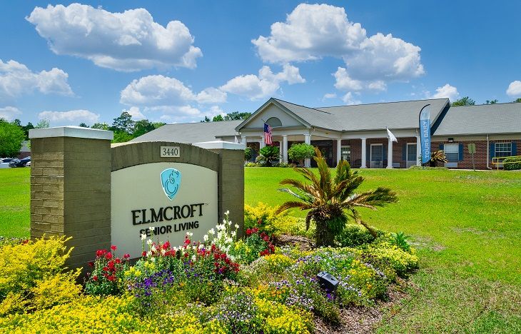 A well-landscaped residential building with a prominent sign and a bright blue sky.