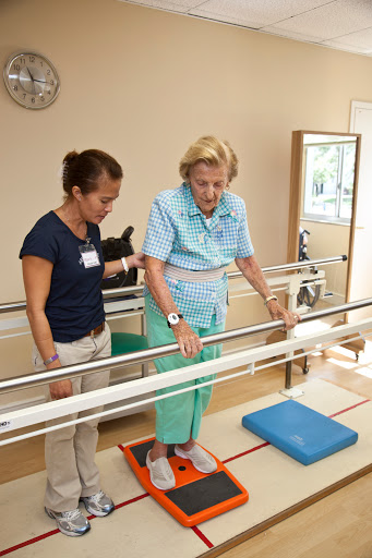 An elderly woman receiving assistance from a therapist during a physical therapy session focused on improving balance and mobility.
