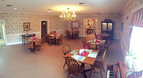 A cozy dining room with wooden tables and chairs, set under a chandelier.