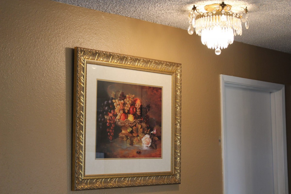 A still life painting in a gold frame adorns a wall beneath an elegant light fixture.