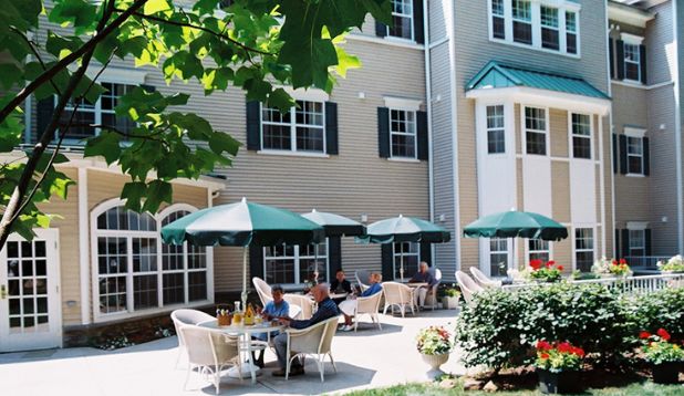 A sunny outdoor patio area with tables, chairs, and umbrellas next to a building.