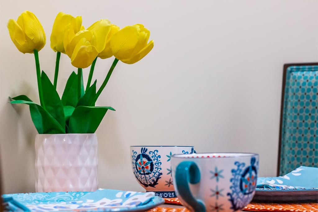 A cozy setup with yellow tulips and patterned tea cups on a table.