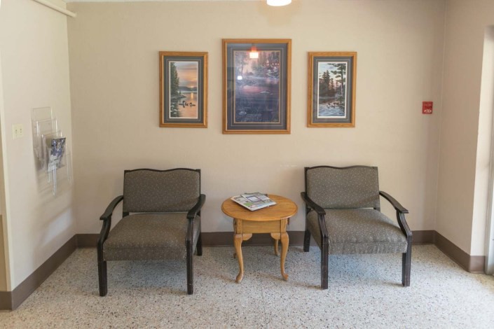 A cozy waiting area with two chairs flanking a small table, adorned with framed artwork on the wall.