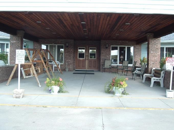 A covered entrance with a swing, chairs, and planters on a concrete porch.