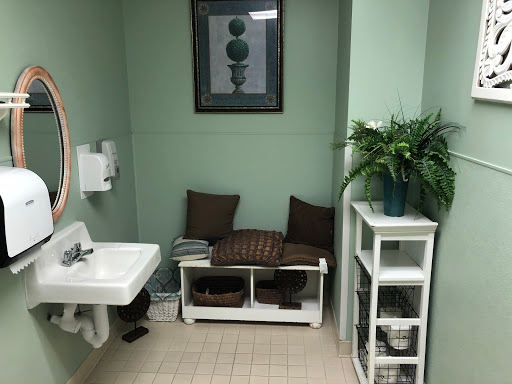 A well-decorated bathroom featuring green walls, a sink, seating area with cushions, and decorative shelves.
