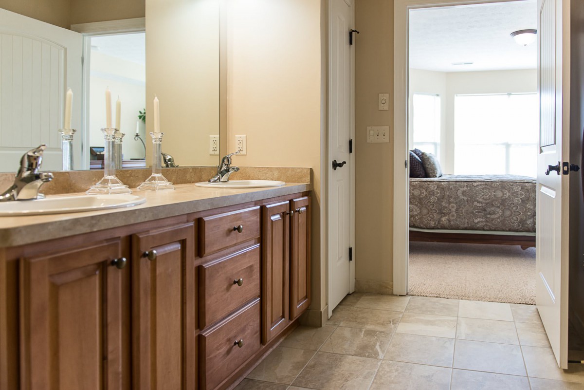 A bathroom featuring a wooden vanity with a mirror and decorative candles, leading into a bedroom.
