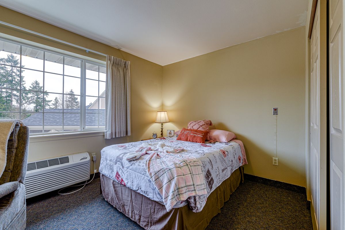 A cozy bedroom with a neatly made bed, soft lighting, and a large window.