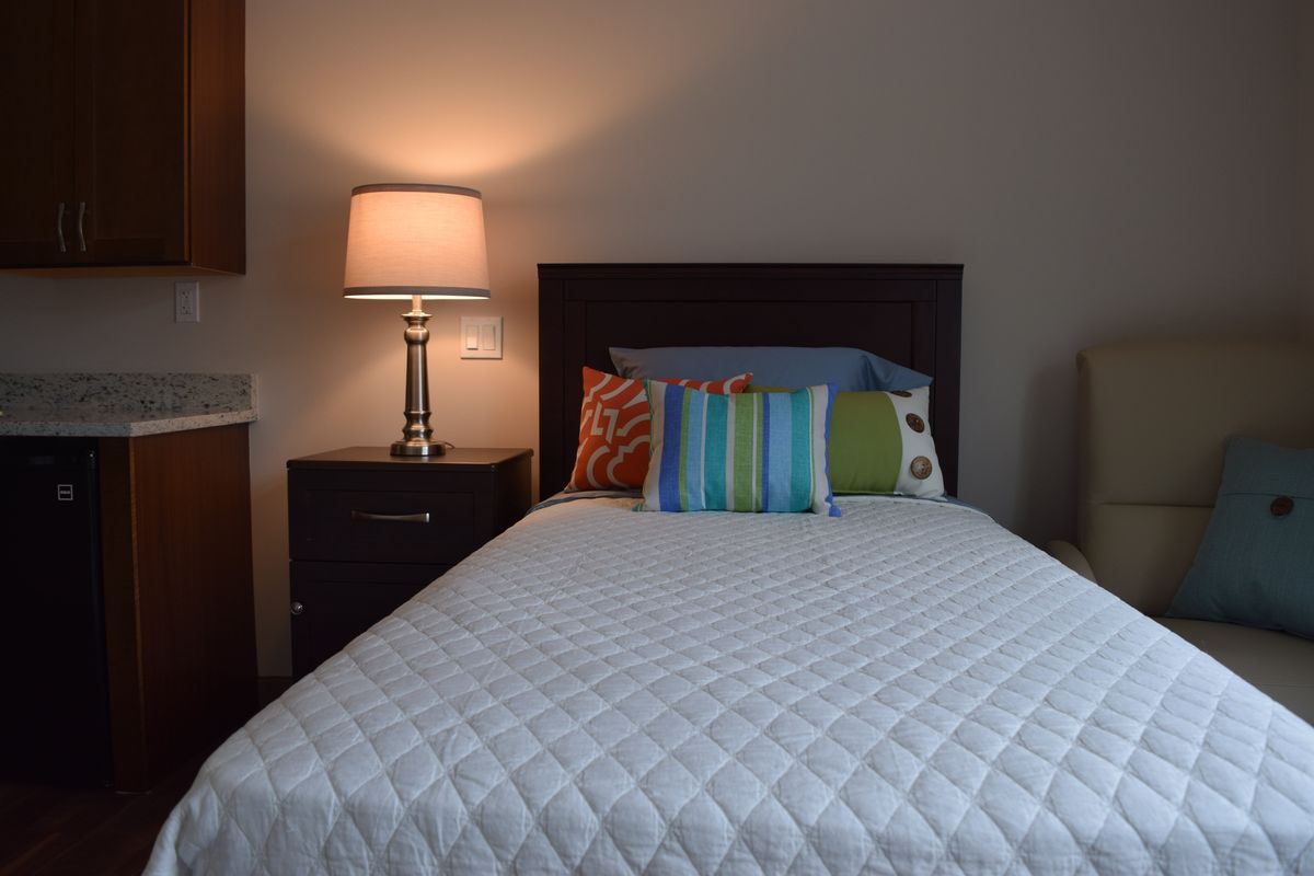 A cozy bedroom with a neatly made bed, decorative pillows, and a lit lamp on the nightstand.