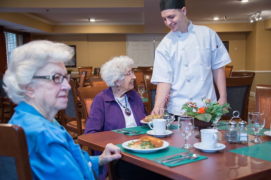 A chef serves food to elderly women in a restaurant setting.