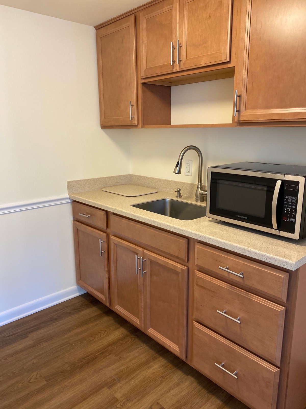 A small kitchenette with wooden cabinets, a microwave, and a sink.