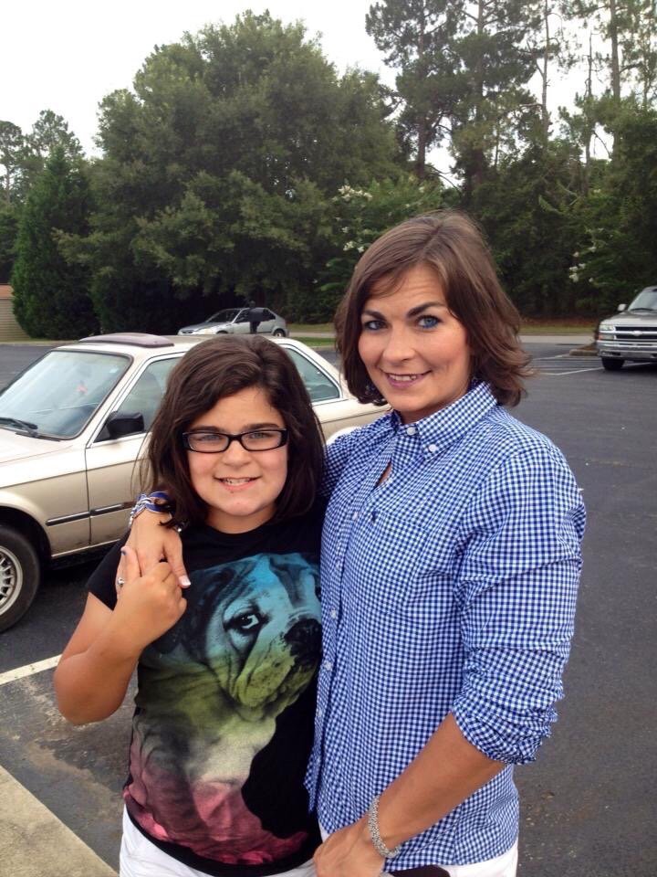 Two people smiling and standing together in a parking lot.
