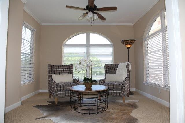 A cozy living room setup with two patterned chairs and a round coffee table, adorned with an orchid centerpiece, under large arched windows and a ceiling fan.