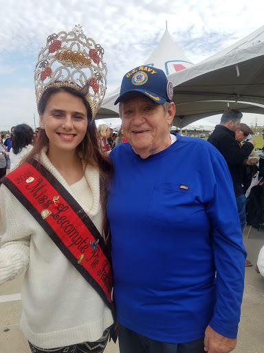 A joyful moment shared between a young woman wearing a sash and a man with a cap at an outdoor event.