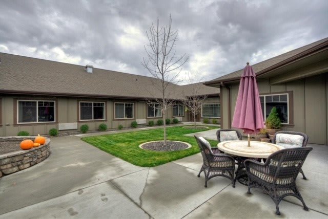 A view of a courtyard with a patio set under an umbrella and a small lawn area on an overcast day.
