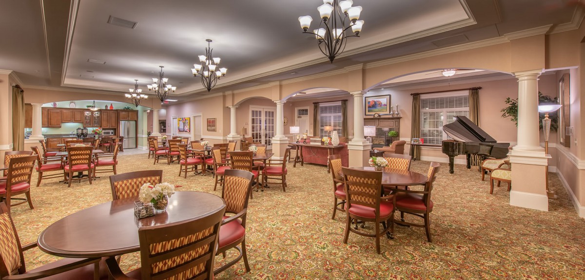 A spacious and elegantly decorated dining area with multiple tables and chairs, illuminated by chandeliers.