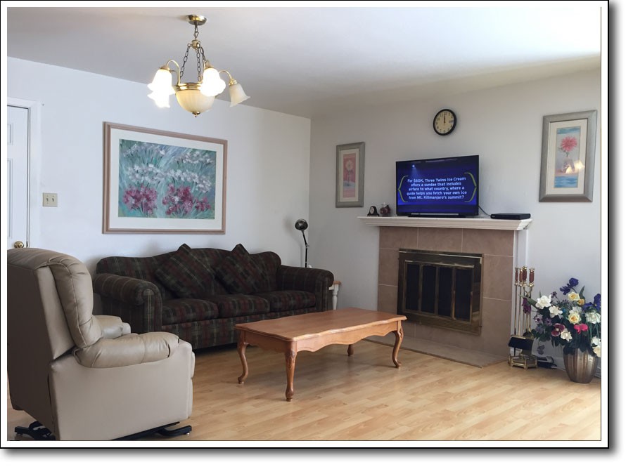 A cozy living room featuring a sofa, armchair, and coffee table, with a fireplace and television mounted above it.
