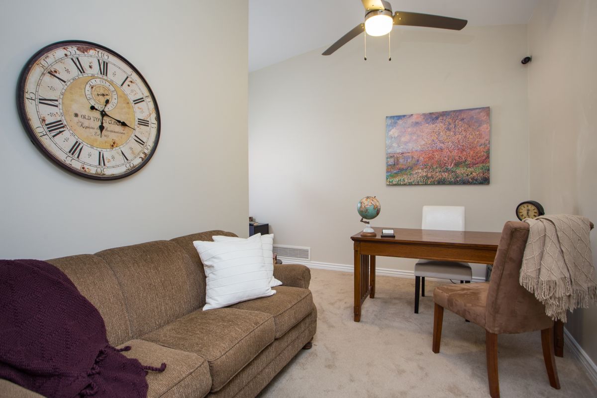 A cozy living area with a sofa and an office desk, featuring a large wall clock and artwork.